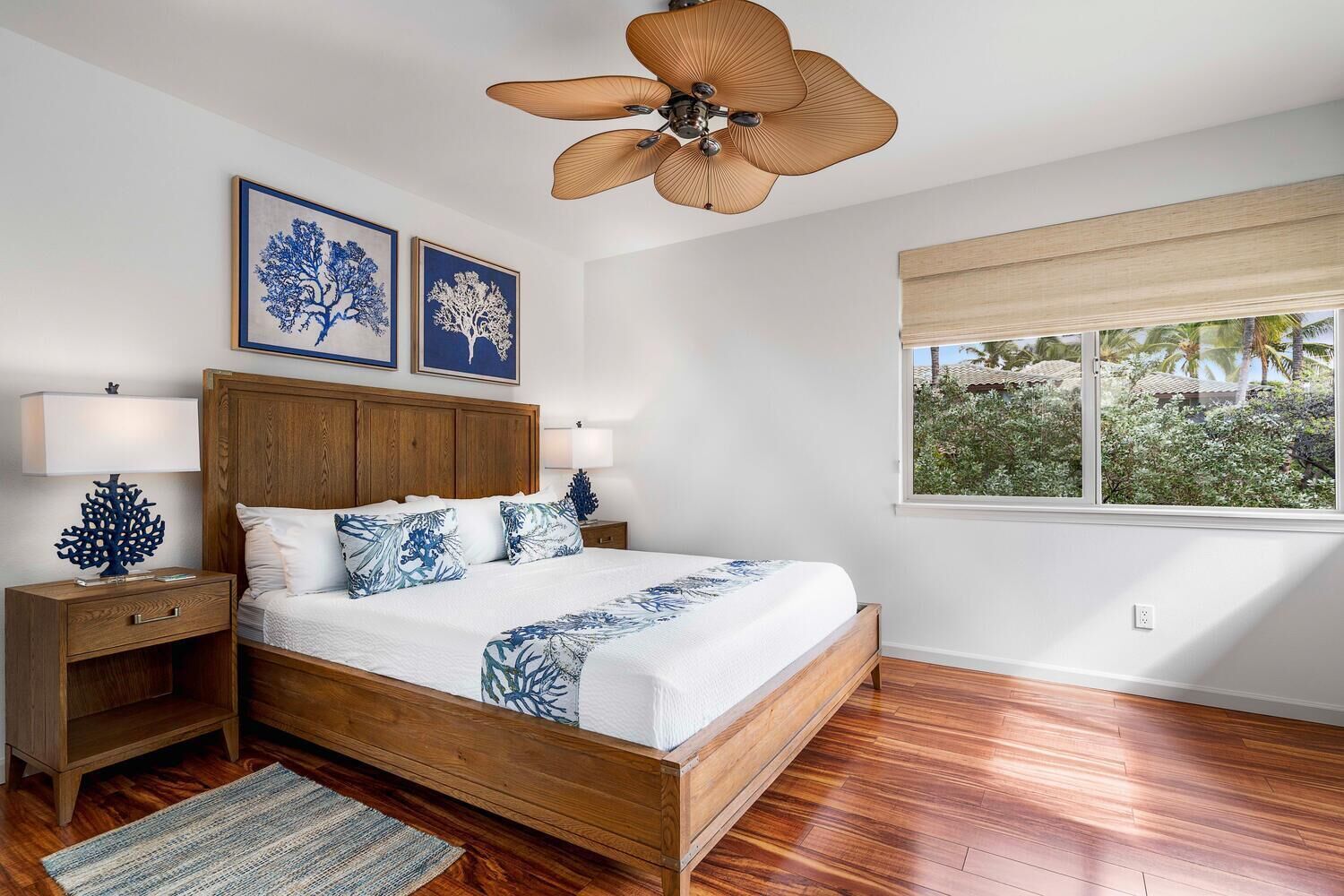 A bedroom with a wooden bed, two nightstands, a ceiling fan, and a window with a view of greenery.