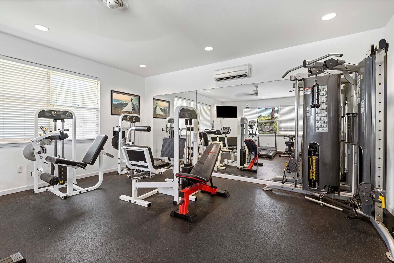 A gym with various exercise machines, a large mirror, and a television on the wall.
