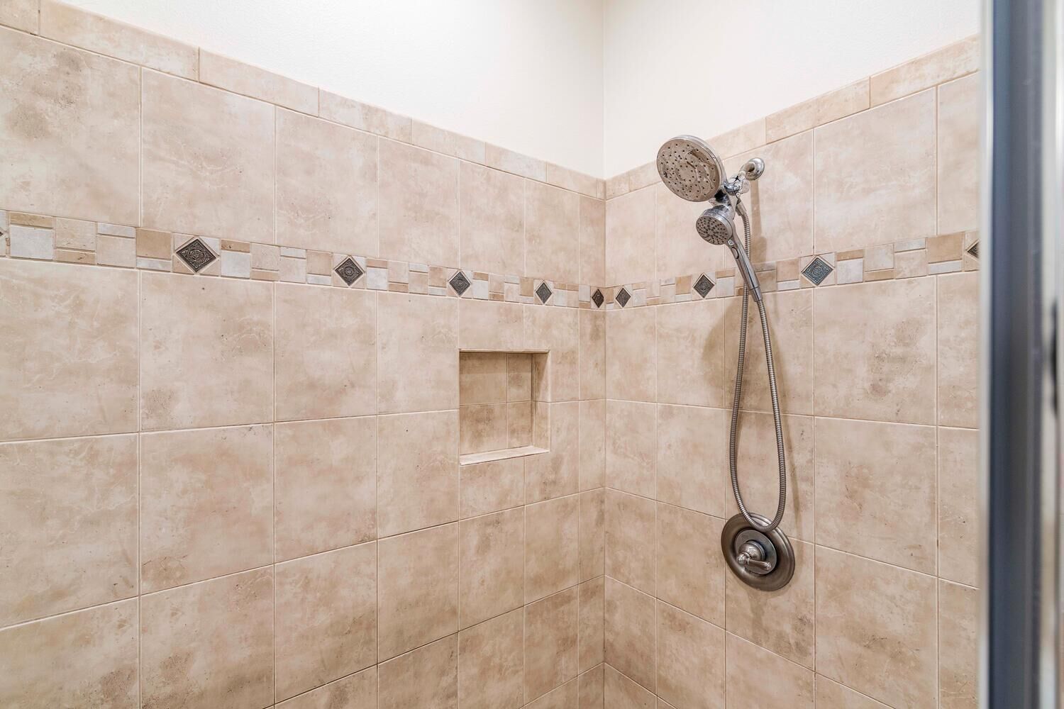 A shower with a handheld showerhead and a wall-mounted control.