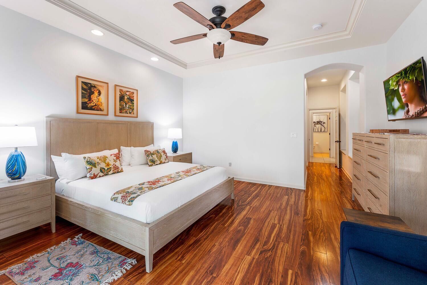 Un dormitorio con una cama de madera, dos mesitas de noche, un ventilador de techo y un televisor sobre un aparador.