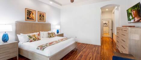 Un dormitorio con una cama de madera, dos mesitas de noche, un ventilador de techo y un televisor sobre un aparador.