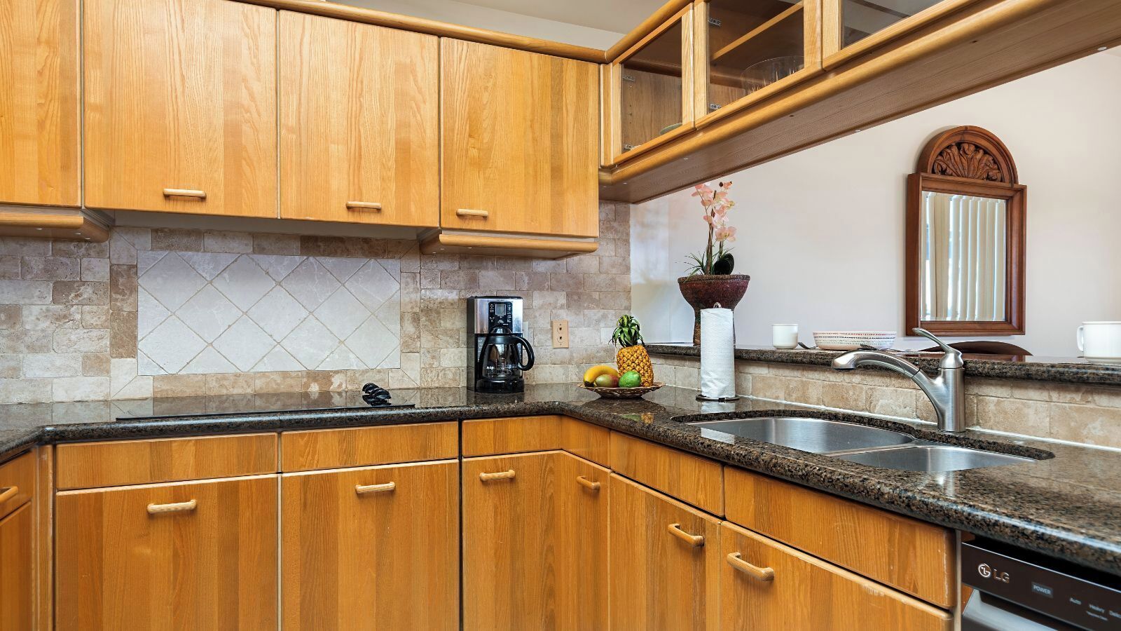 A kitchen with wooden cabinets, a granite countertop, a coffee maker, a fruit bowl, and a sink.