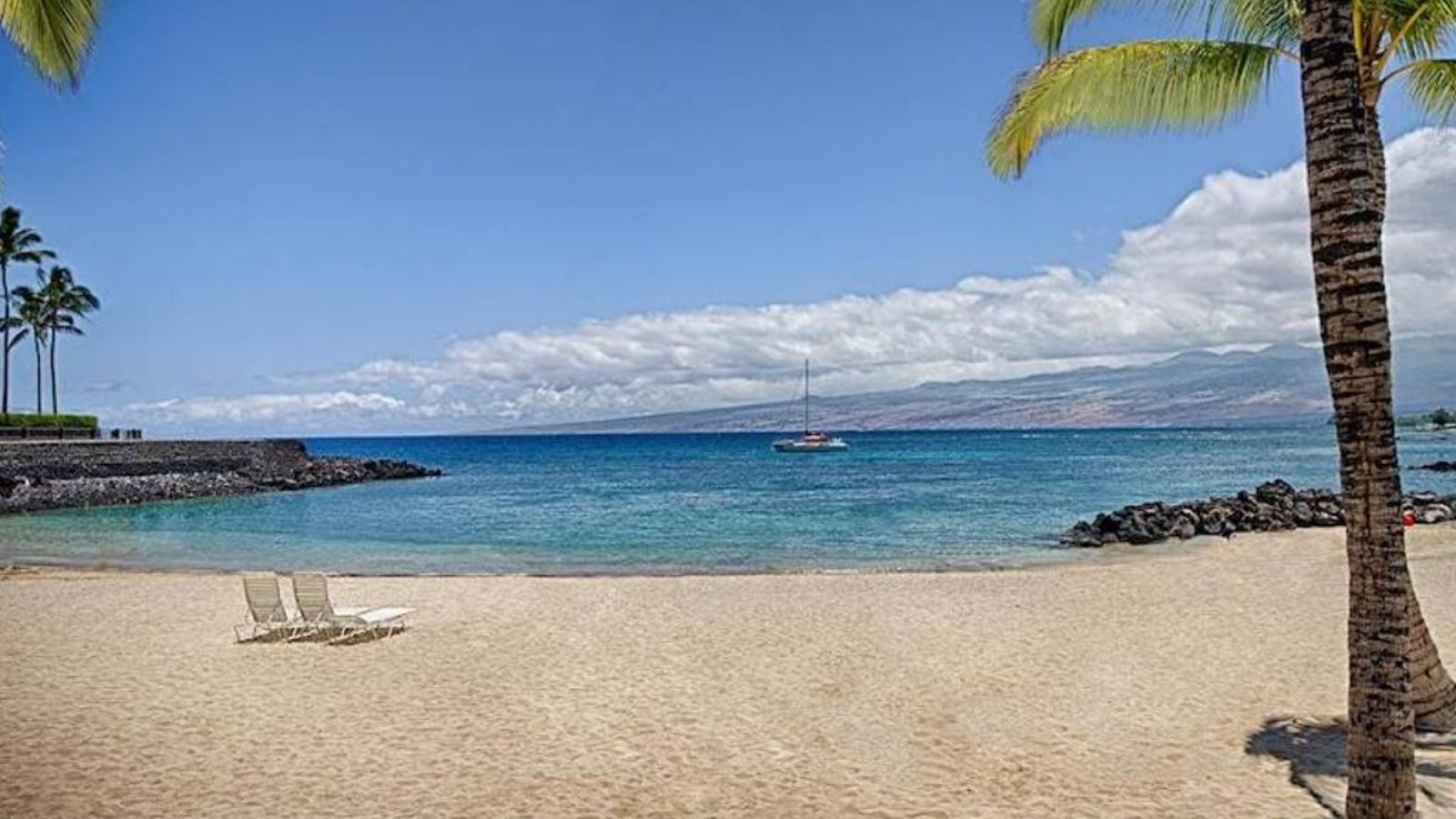 A beach with two lounge chairs, a clear blue sky, and a sailboat in the distance.