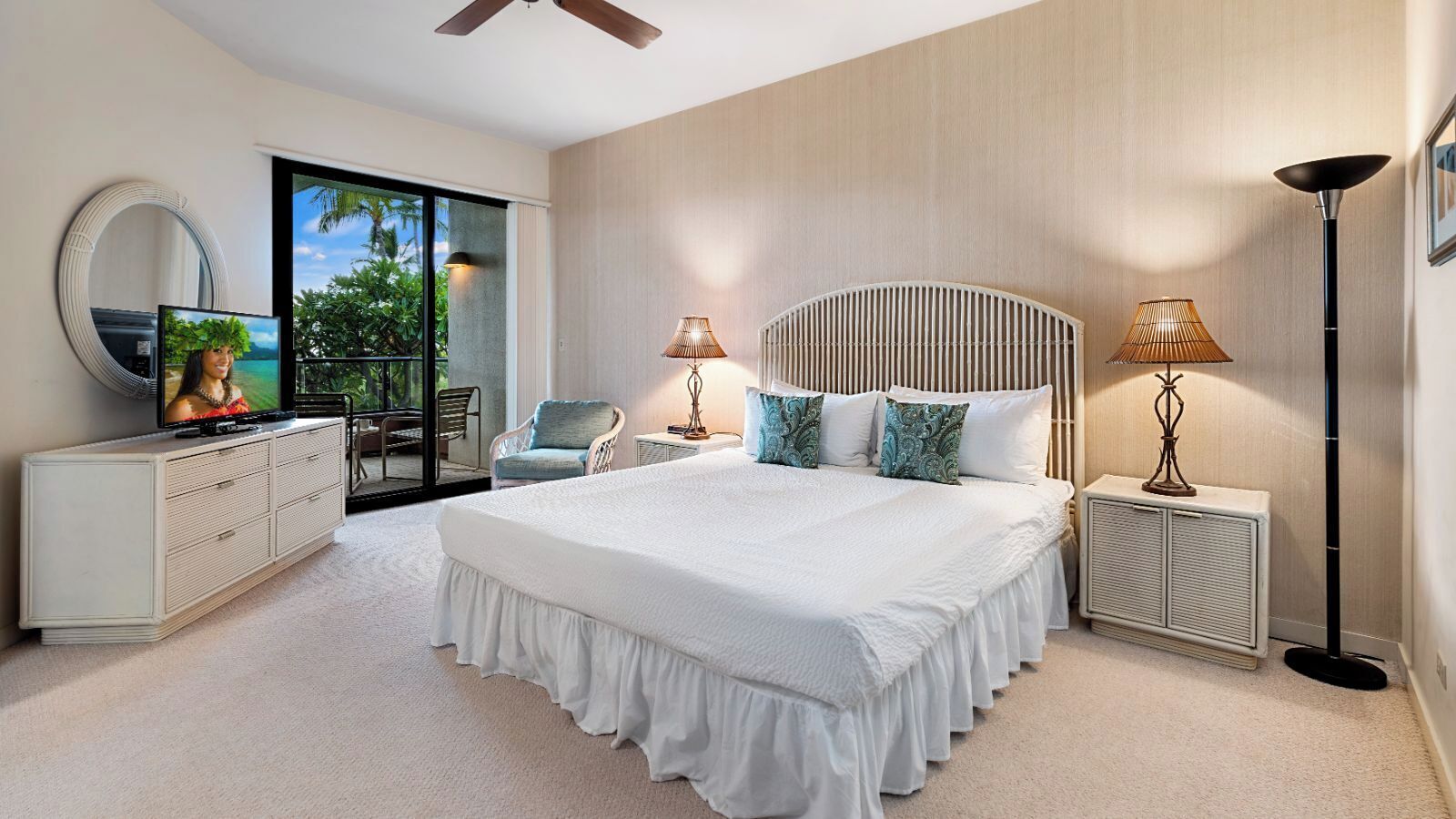 A bedroom with a large bed, a television, a chair, two bedside tables with lamps, and a view of greenery outside.