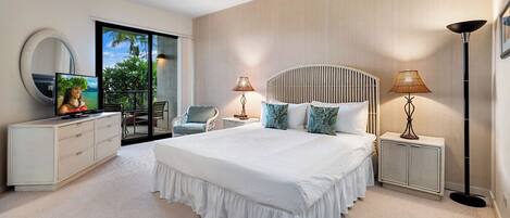 A bedroom with a large bed, a television, a chair, two bedside tables with lamps, and a view of greenery outside.
