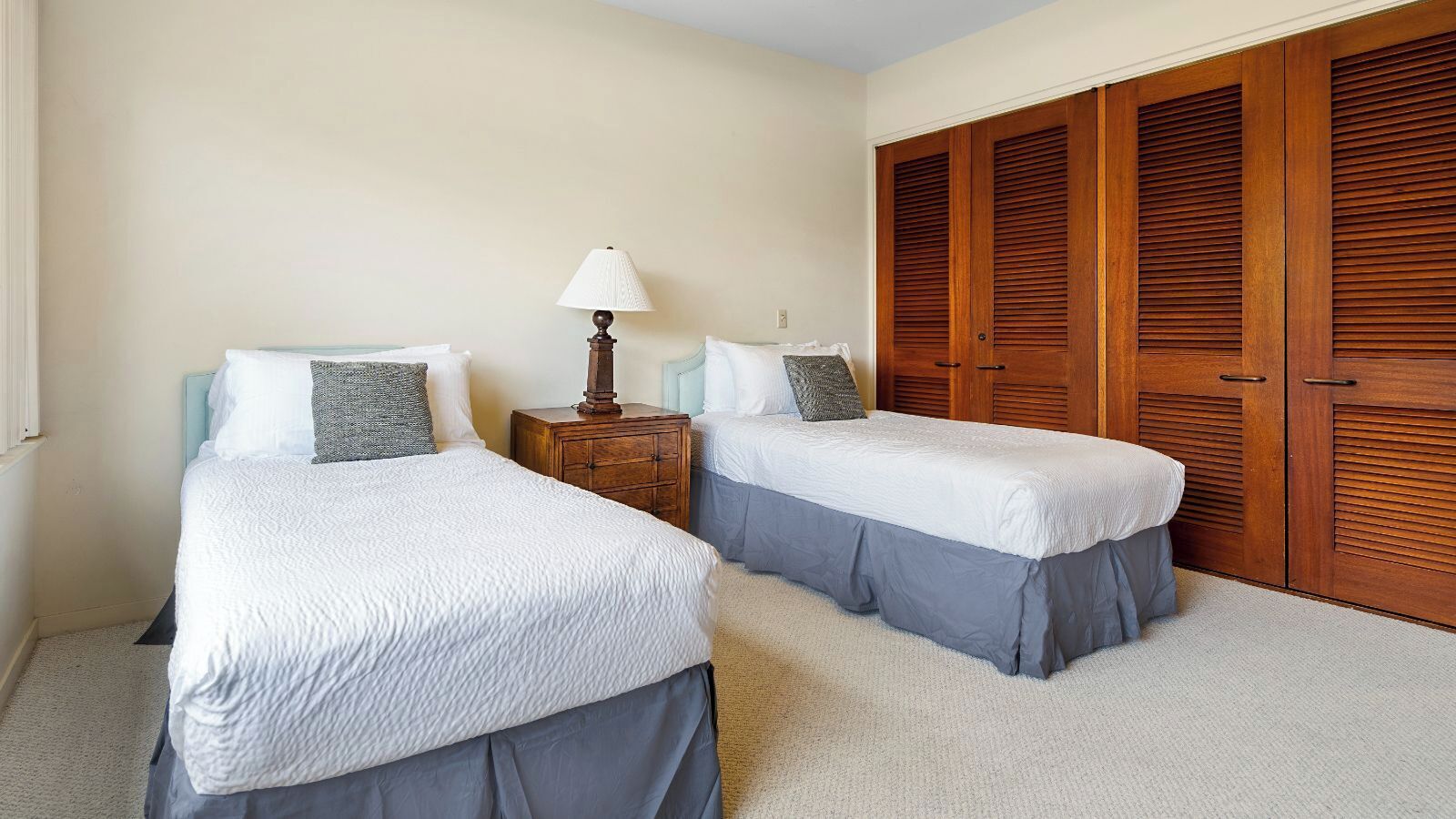 A hotel room with two beds, a nightstand with a lamp, and wooden wardrobes.