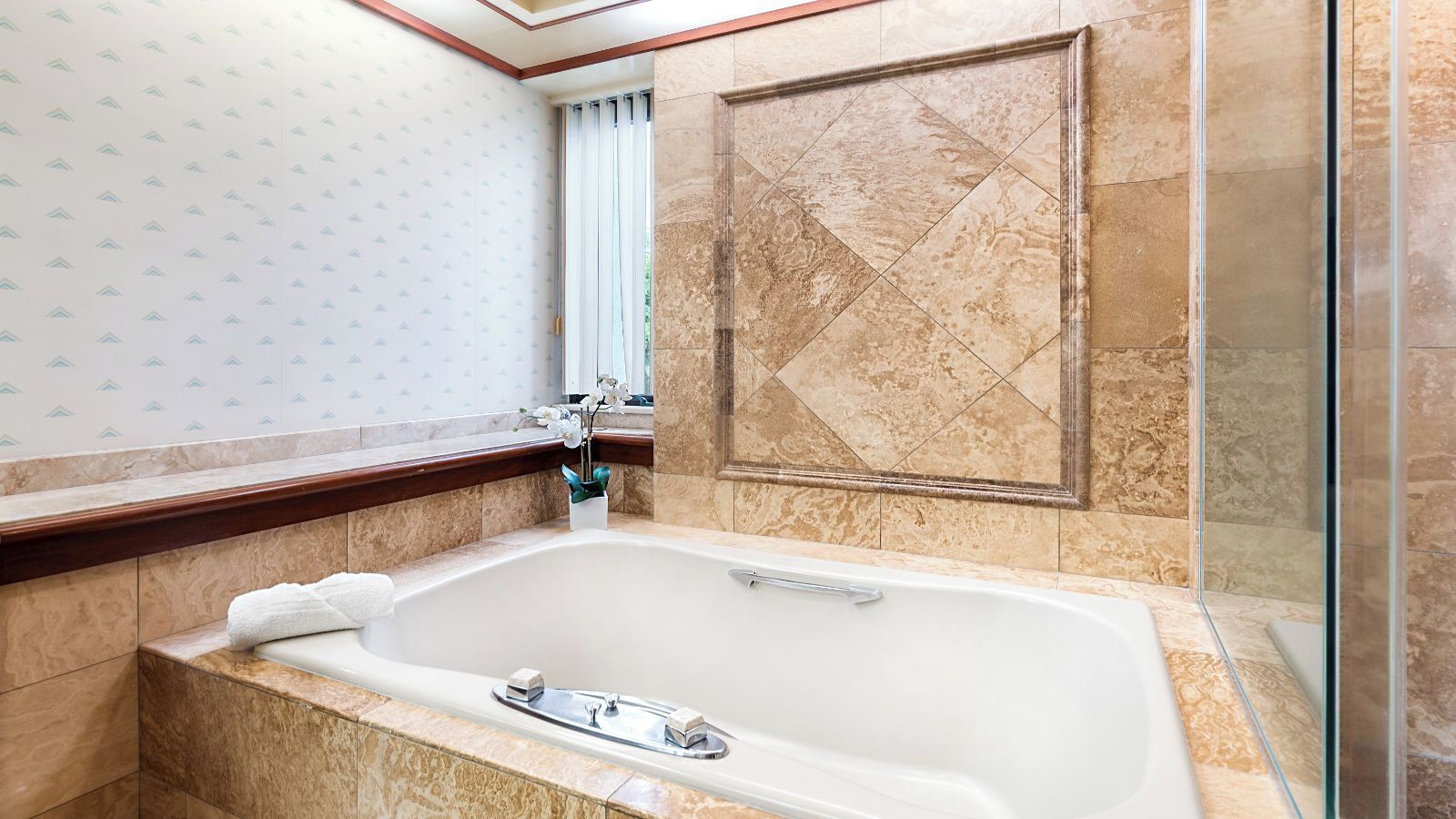 A bathroom with a large bathtub, a glass shower enclosure, and patterned wallpaper.