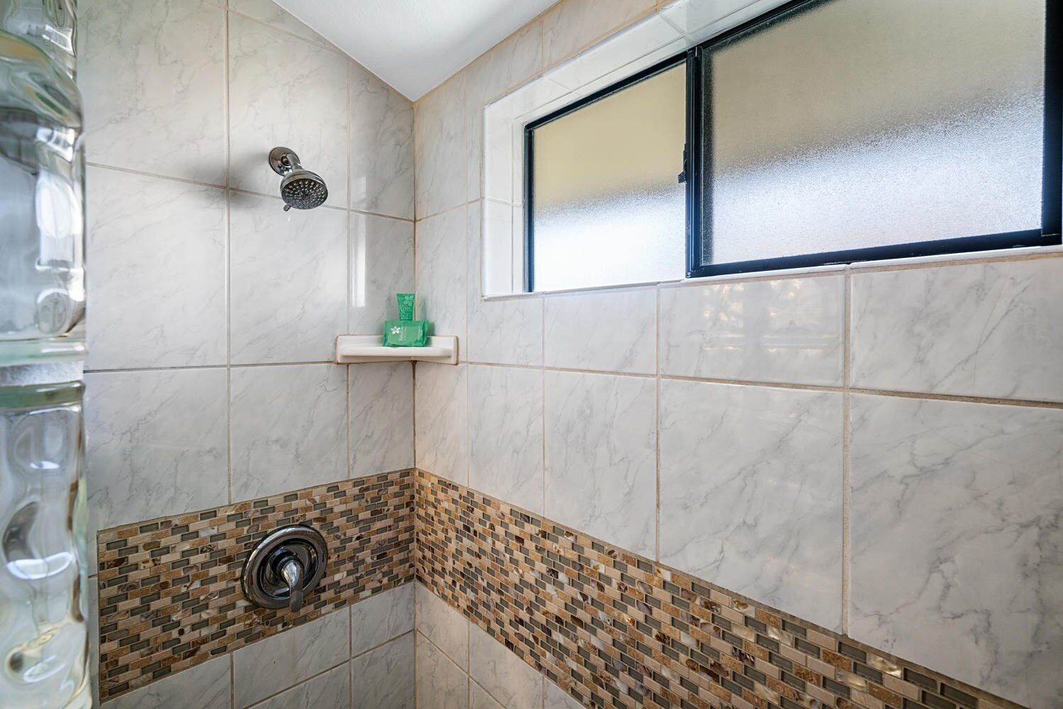 A bathroom with a shower, a window, and a sink with a tiled backsplash.
