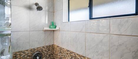 A bathroom with a shower, a window, and a sink with a tiled backsplash.