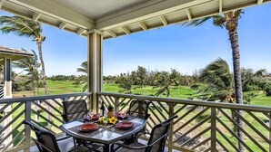 A covered outdoor dining area with a table set for two, overlooking a golf course. - 2 Bdrm Plus Loft - AC & Wifi - Concierge Included - Lanai!! - Vrkcv (Waikoloa)