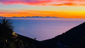 A coastal landscape with a sunset over the sea, mountains in the distance, and a silhouette of a palm tree. - Quiet apartment in front of Corsica (Colle D'orano)