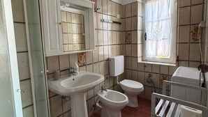 A bathroom with a sink, bidet, toilet, and a window with a curtain. - Quiet apartment in front of Corsica (Colle D'orano)