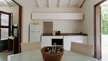 Una cocina moderna con armarios blancos, un refrigerador y un comedor con una mesa de vidrio y sillas de mimbre.