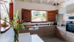 A modern kitchen with wooden cabinets, a built-in oven, and a window with wooden shutters. - Habitation Tabanon (Petit-Bourg)