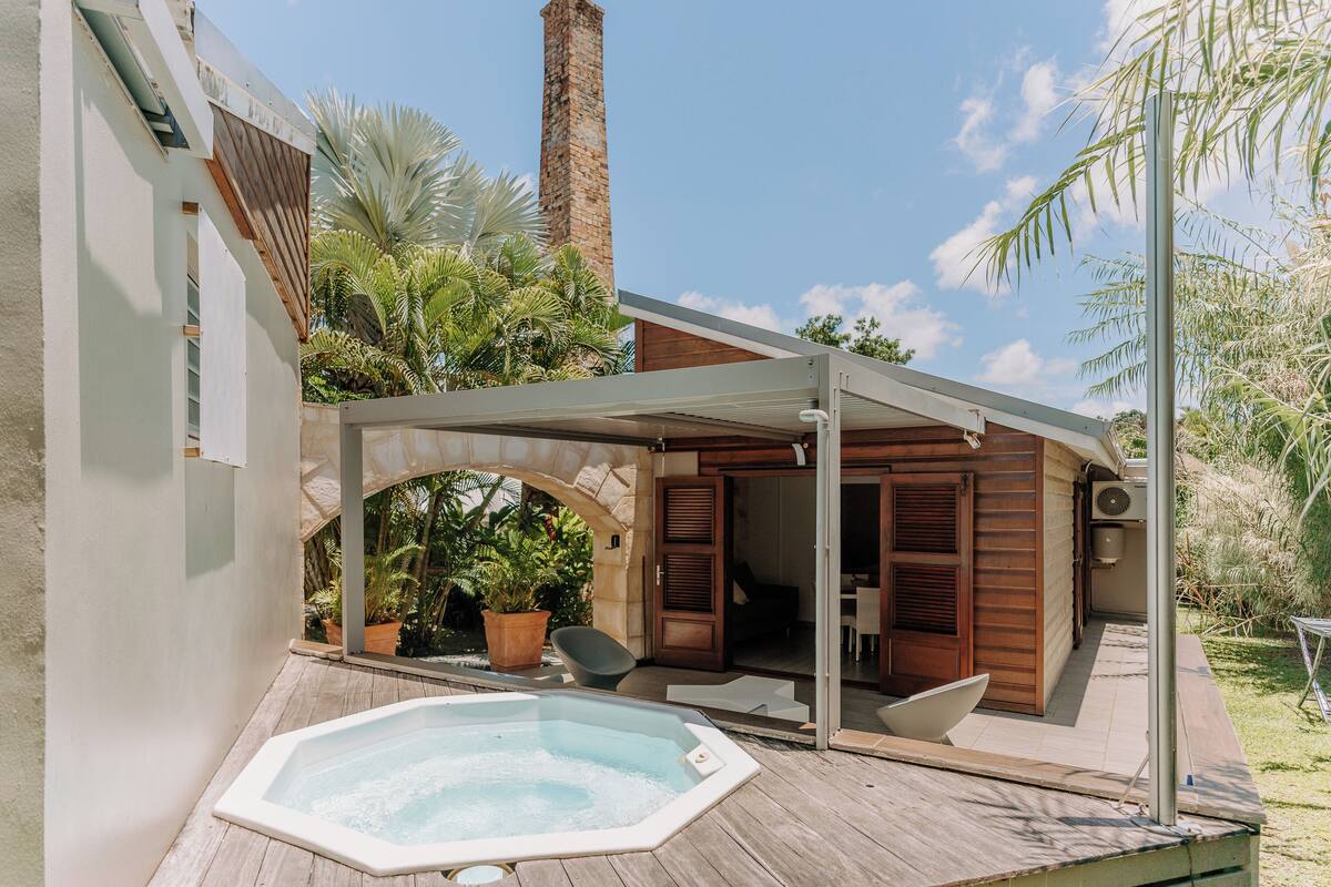 A covered outdoor area with a hot tub, wooden deck, and a patio with chairs and a table.