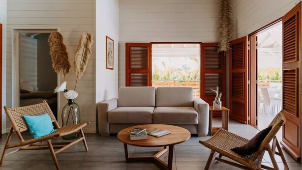 A room with a sofa, two wicker chairs, a coffee table, and a view through open wooden shutters to an outdoor area. - Habitation Tabanon (Petit-Bourg)