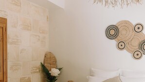 A bedroom with a bed, a wooden bench, a woven rug, a vase with flowers, and a wall with a textured pattern. - Habitation Tabanon (Petit-Bourg)