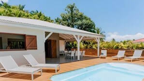 A poolside area with lounge chairs, a covered seating area, and a view of a building with wooden shutters. - Habitation Tabanon (Petit-Bourg)