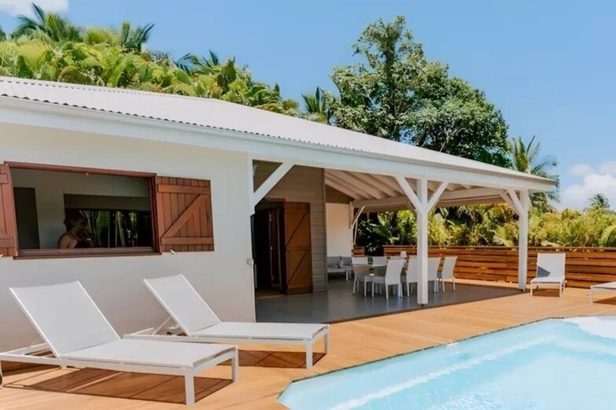 A poolside area with lounge chairs, a covered seating area, and a view of a building with wooden shutters.
