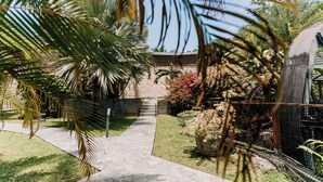A paved pathway leading to a building with a stone wall and a water feature. - Habitation Tabanon (Petit-Bourg)