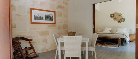 A dining area with a table and chairs, a rocking chair, a bed with a headboard, and a wall-mounted picture frame.
