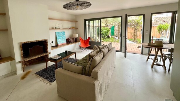 A modern living room with a fireplace, a sofa, a dining table, and a bright window overlooking a garden. - Charming 2-bedroom house in La Flotte-en-Ré, near beach and port (La Flotte)