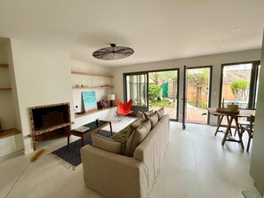 A modern living room with a fireplace, a sofa, a dining table, and a bright window overlooking a garden. - Charming 2-bedroom house in La Flotte-en-Ré, near the beach and harbor (La Flotte)