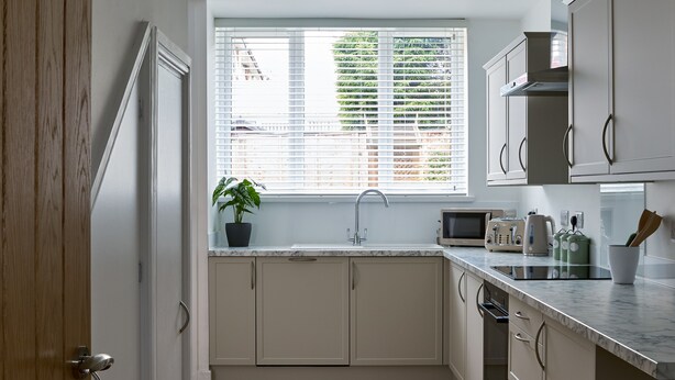 Una cocina moderna con armarios blancos, una ventana con persianas, un fregadero, un microondas y una encimera con diversos objetos.