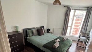 Un dormitorio con cama, cómoda, radiador, escritorio y ventana con cortinas.