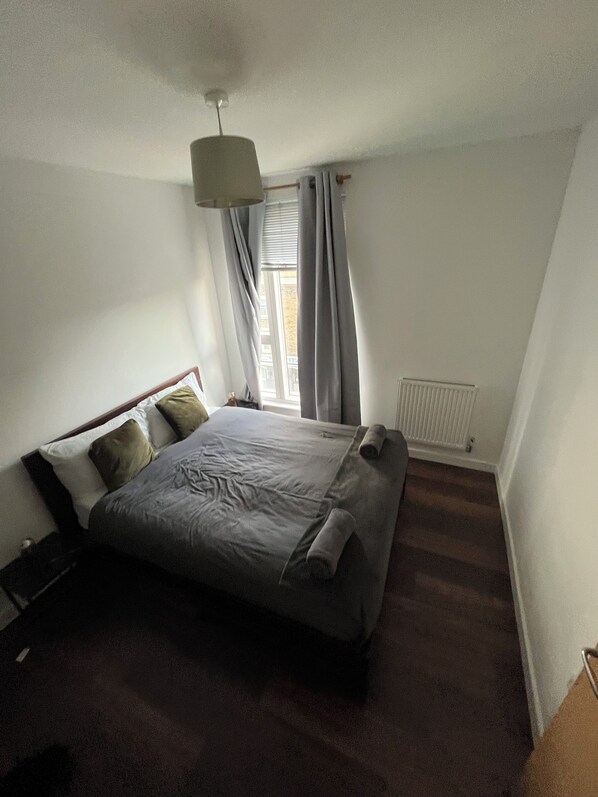 A bedroom with a bed, a radiator, and a window with curtains.