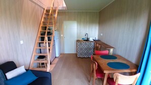 Un espai vital compacte amb una escala de fusta, un petit cuina, una zona de menjador amb taula i cadires, i un sofà amb coixins.