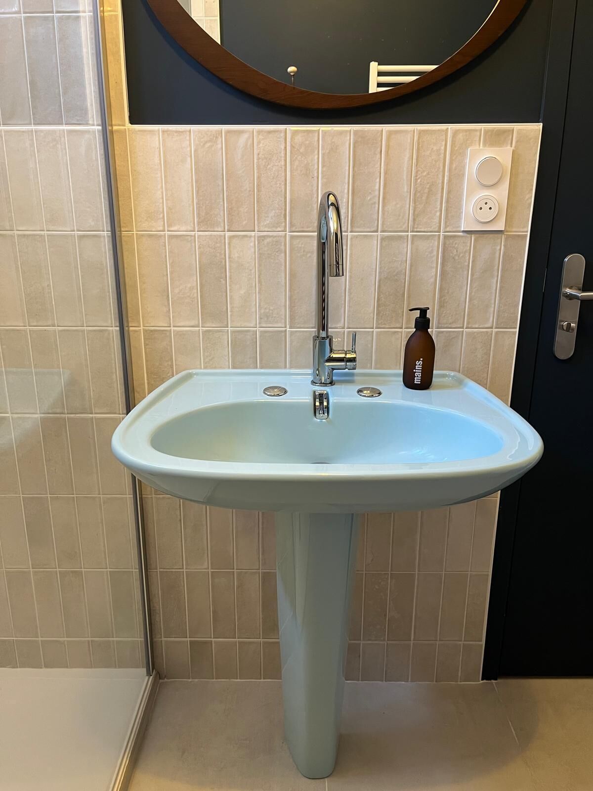 A bathroom with a pedestal sink, a mirror, and a bottle of soap.
