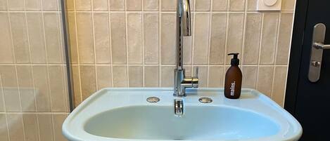 Un baño con lavamanos pedestal, espejo y botella de jabón.