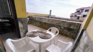 Une terrasse avec une table ronde et quatre chaises en plastique blanc, chacune agrémentée d’un set de table en fibres tressées.