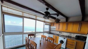 A kitchen with a dining table, chairs, a ceiling fan, and a view of the ocean through large windows. - Atlantic Dream Sunset (Mesa del Mar)