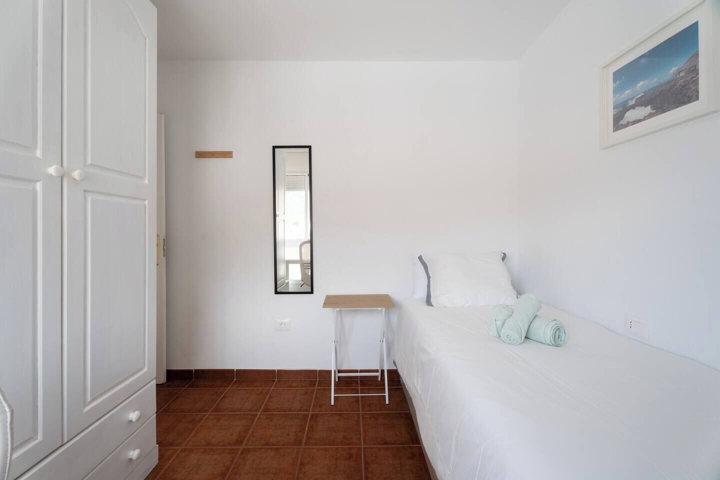 A bedroom with a bed, a nightstand, a wardrobe, a mirror, and a picture on the wall.