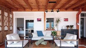 Un salon moderne avec un plafond en bois, des canapés blancs, une table basse et une vue sur la mer grâce à de grandes fenêtres.