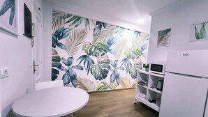 Una cocina compacta con una mesa redonda, armarios blancos y un papel tapiz con motivos de hojas tropicales.