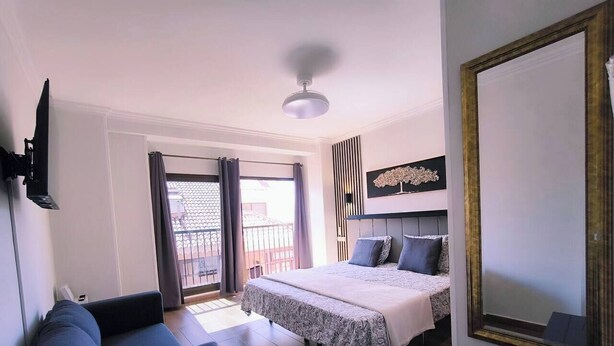 Un dormitorio con cama, sofá, televisión y balcón.