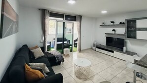 A modern living room with a sofa, a coffee table, a TV, and a sliding glass door leading to a balcony. - Argos Sunset Apartment (Candelaria)