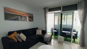 A living room with a black sofa, a round coffee table, and a glass door leading to an outdoor area with a table and chairs. - Argos Sunset Apartment (Candelaria)