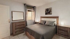 A bedroom with a bed, two nightstands, a dresser, a window with curtains, and a wall-mounted artwork. - Argos Sunset Apartment (Candelaria)
