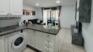 A modern kitchen with granite countertops, a built-in washing machine, and a dining area with a view. - Argos Sunset Apartment (Candelaria)