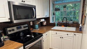 A kitchen with white cabinets, a stainless steel microwave, a black stove, and a window with a view of greenery.