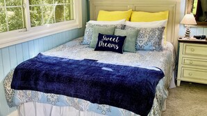 A bedroom with a bed, pillows, a nightstand, a lamp, and a window.