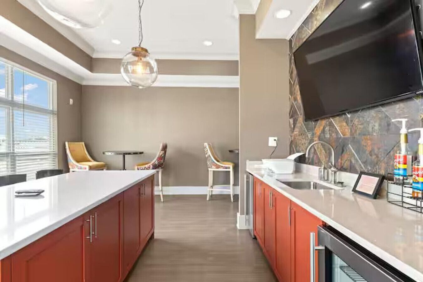 A modern kitchen with a large island, red cabinets, and a flat-screen TV mounted above the island.