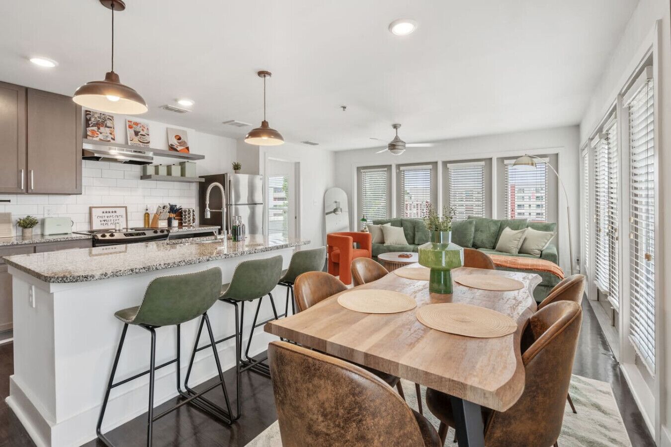 A modern kitchen with a central island, bar stools, and a dining table with placemats.