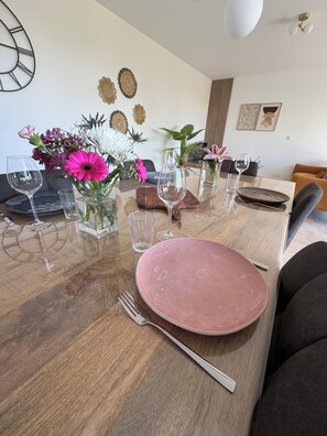 Une table à manger dressée avec des assiettes roses, des verres transparents et une fourchette.
