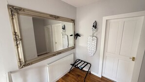 Een kamer met een grote, versierde spiegel, een radiator, een deur en een wandmontabele strijkplank.