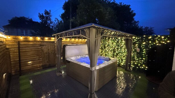 Een hottub met een houten terras en een overdekt gebied met lichtjes.